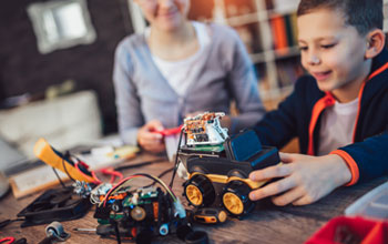 a boy holding a remote controlled car while the girl in the background controls the car
