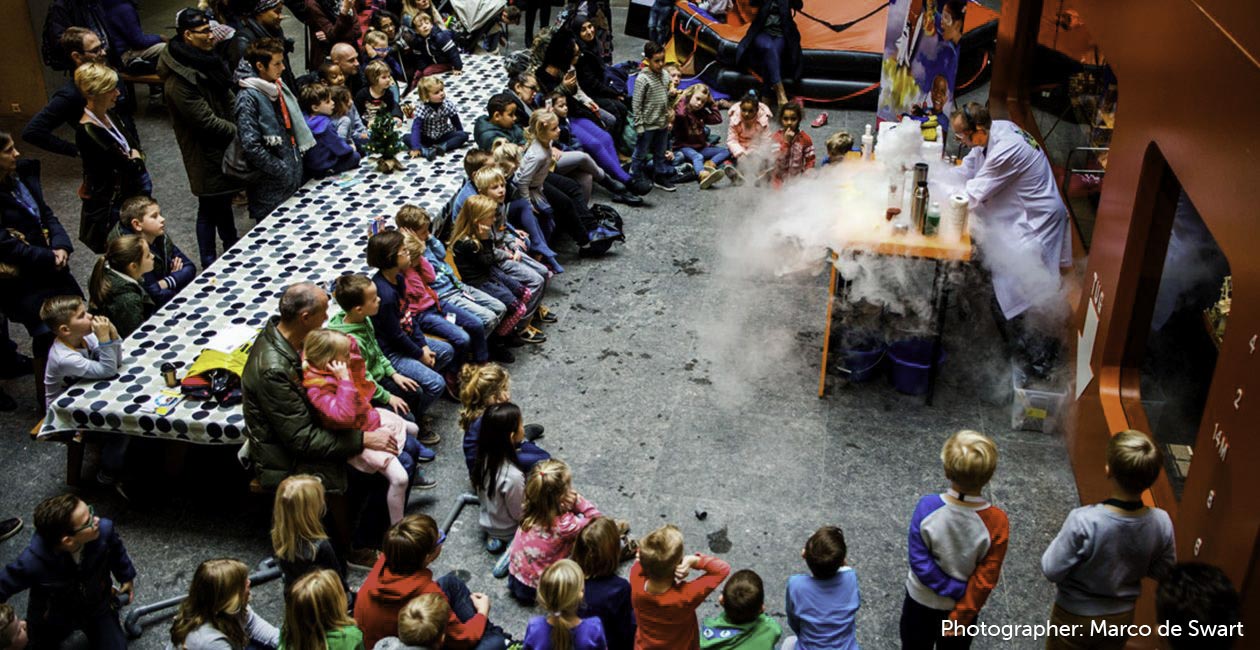 Mad scientist performing on a table with smoke, beakers, in front of children
