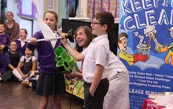 Mad Scientist holding a toilet paper roll gun while kids are holding a plunger with a roll of toilet paper through it.
