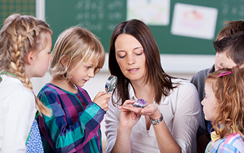 Kids gathered around teacher holding a geode with the boy next to her looking through magnifying glass