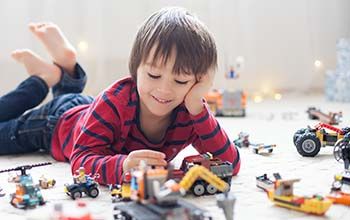 Boy lying on the ground playing with Lego vehicles