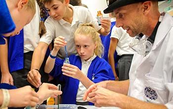 Kids pouring colored liquid from a pipette onto a tray of ice