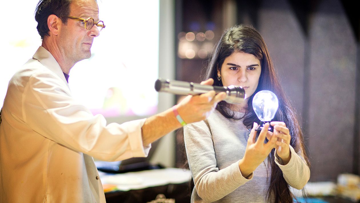 Mad scientist holding flash light point it at a light bulb that a girl is holding