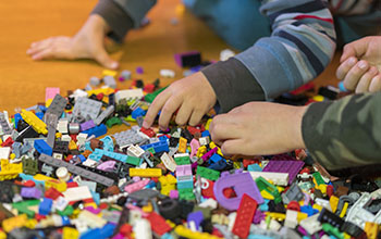 Close up of hands playing with colorful plastic bricks on the floor.
