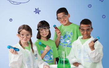 4 kids 2 of which are in lab coats all holding test tubes filled with liquid and one flask with green liquid inside.